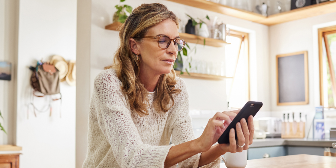 Eine Frau in ihrem Zuhause hält ein Smartphone mit einer digitaler Versicherungskarte zur Kundenbindung in der Hand